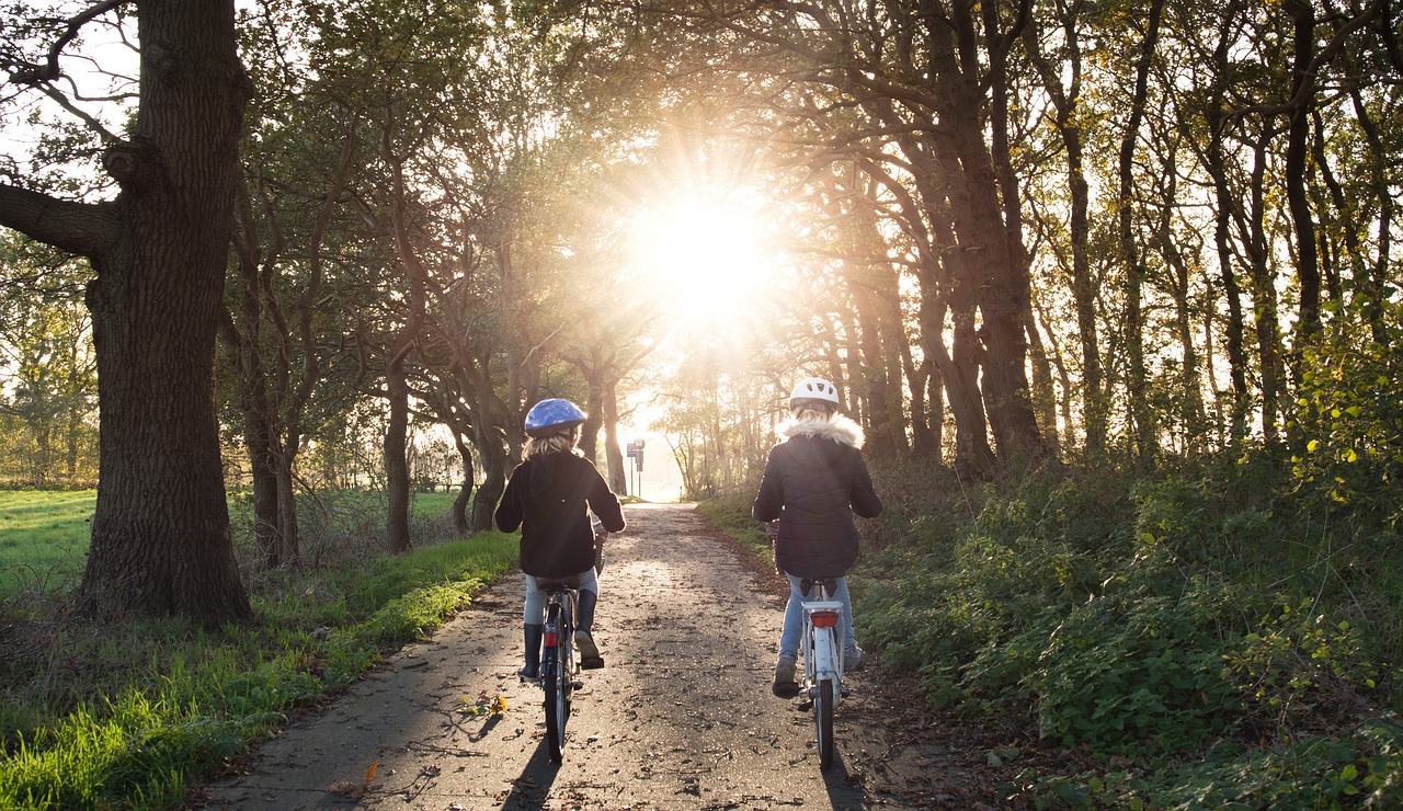 Zwei Mädchen fahren auf einem Fahrrad durch den Wald. Die Abendsonne fällt ein.