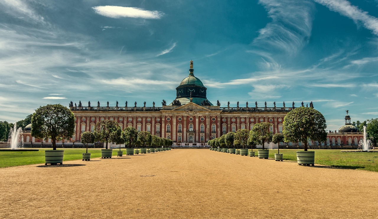Barockes Schloss mit zentraler Kuppel, symmetrischem Gartenweg und beidseitig gesäumten Kübelbäumen.