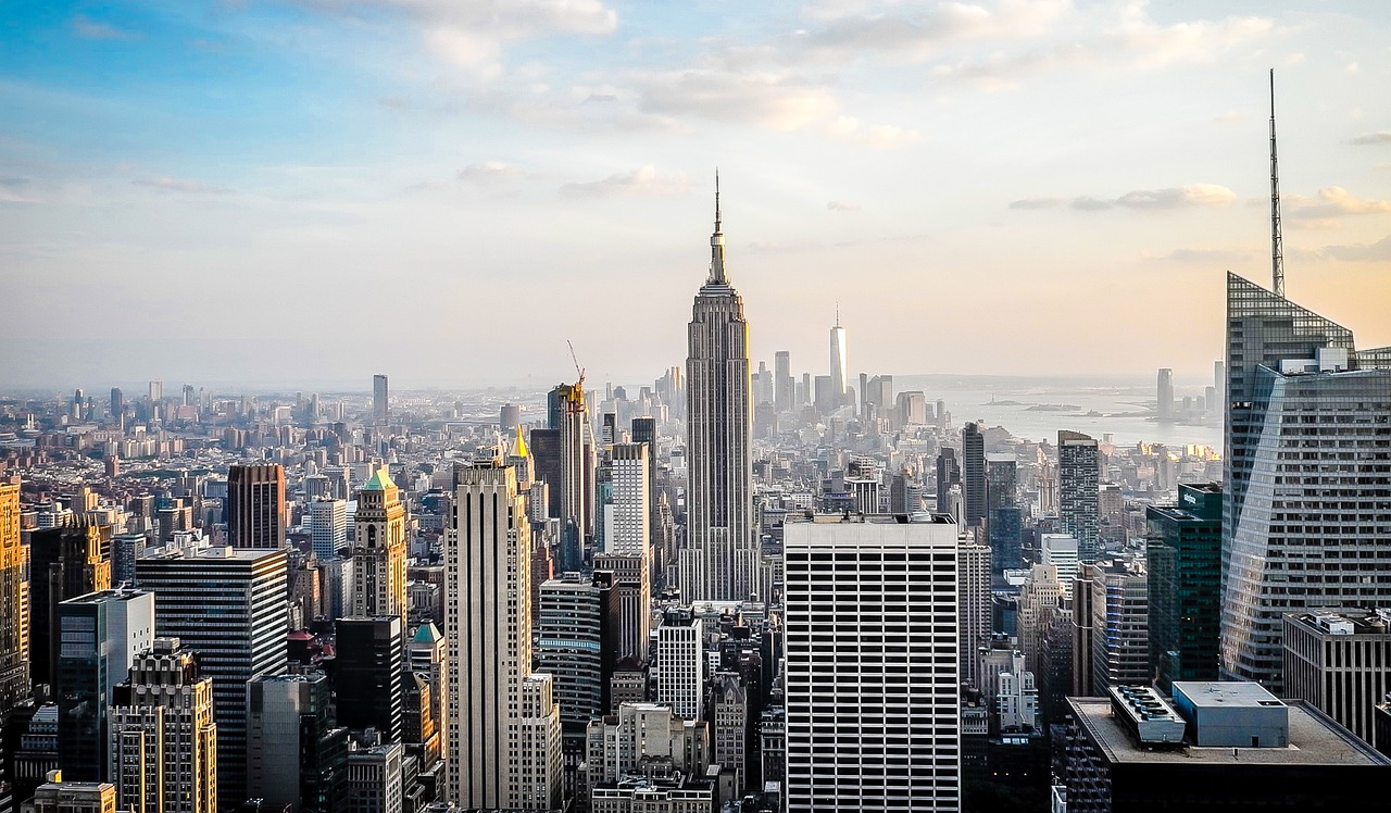 Städtisches Panorama von New York City mit zahlreichen Hochhäusern, im Zentrum das Empire State Building, im Hintergrund Wasserfläche und ferne Skyline.