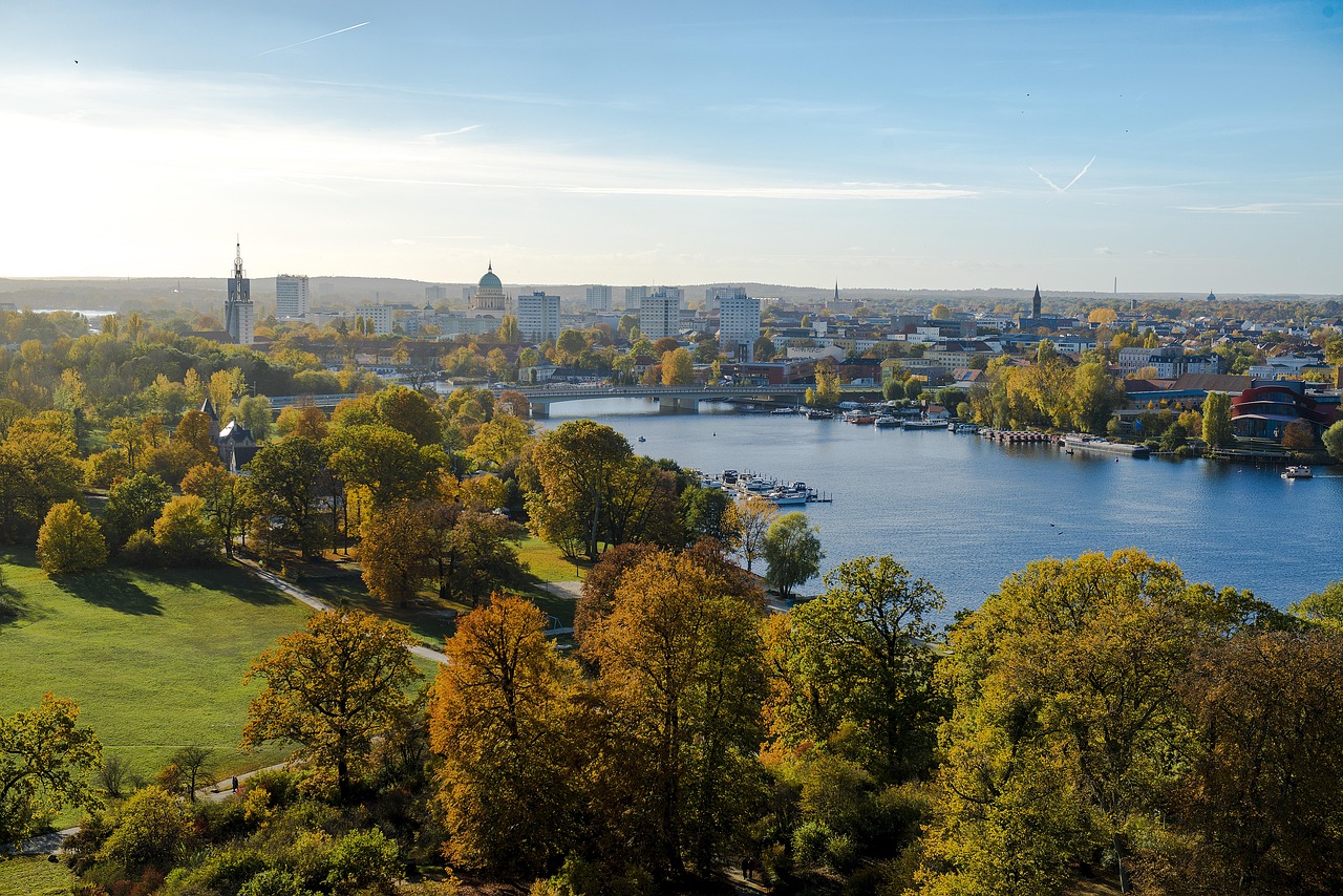Stadtansicht mit Fluss, herbstlich gefärbtem Park im Vordergrund und markanter Kuppel sowie Hochhäusern in der Skyline.