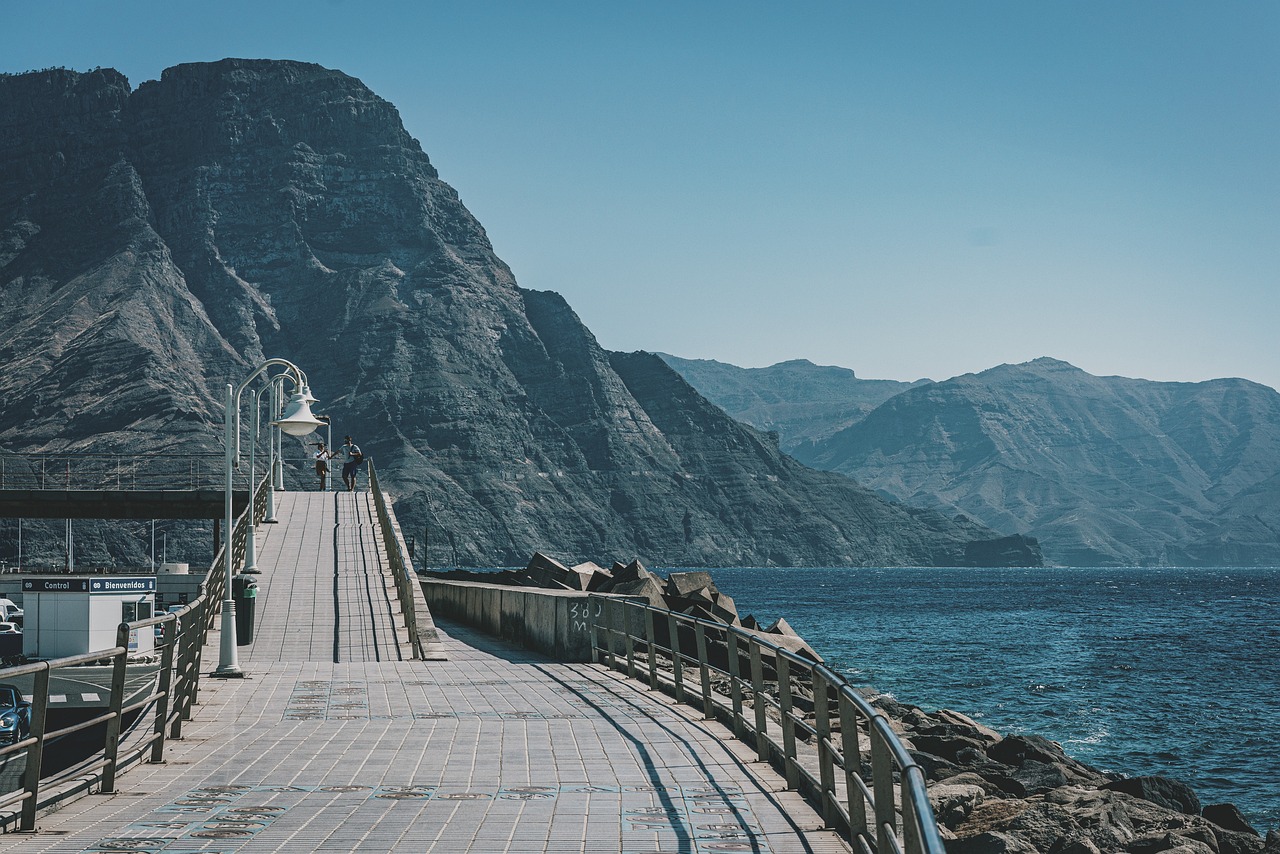 Gepflasterte Promenade mit Geländer und Straßenlampen vor steilen Felsklippen am Meer.